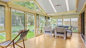 A spacious room with large glass doors leading to a garden, furnished with wicker chairs and a sofa.