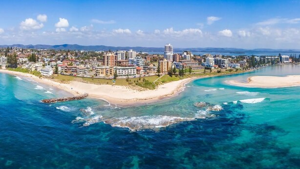 A coastal cityscape with a beach, clear blue waters, and a variety of buildings including residential and commercial structures.