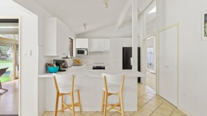 A modern kitchen with white cabinetry, a central island with bar stools, a microwave, and a refrigerator.