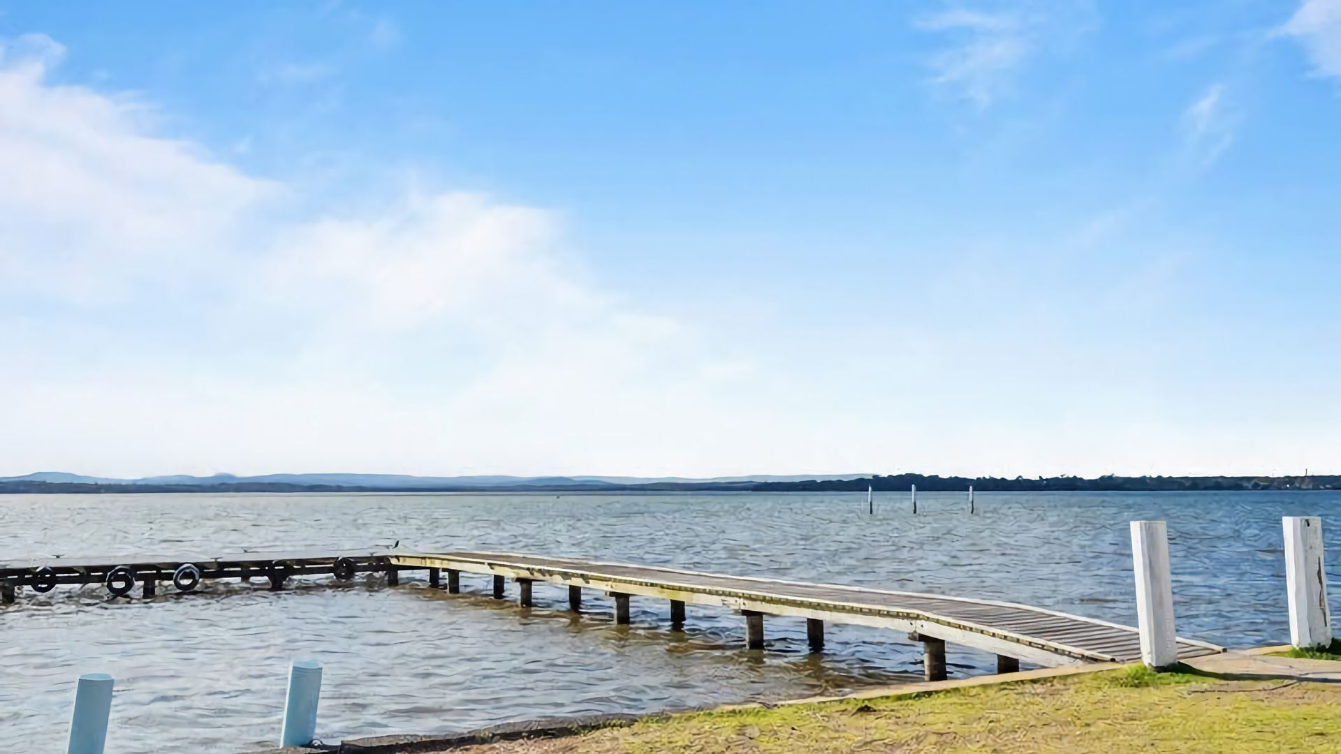 Un muelle de madera se extiende sobre un lago tranquilo bajo un cielo despejado.