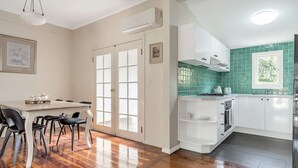 A kitchen with white cabinets, a green tiled backsplash, and a dining area with a table and chairs. - The Katoomba Nest Blue Mountains Escape (Katoomba)