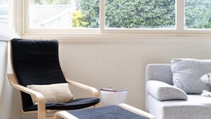 A room with a black chair, a grey sofa, and a window with a view of greenery. - The Katoomba Nest Blue Mountains Escape (Katoomba)