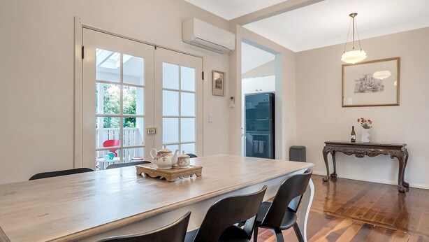 A dining area with a long table, chairs, and a small side table with a bottle and flowers. - The Katoomba Nest Blue Mountains Escape (Katoomba)