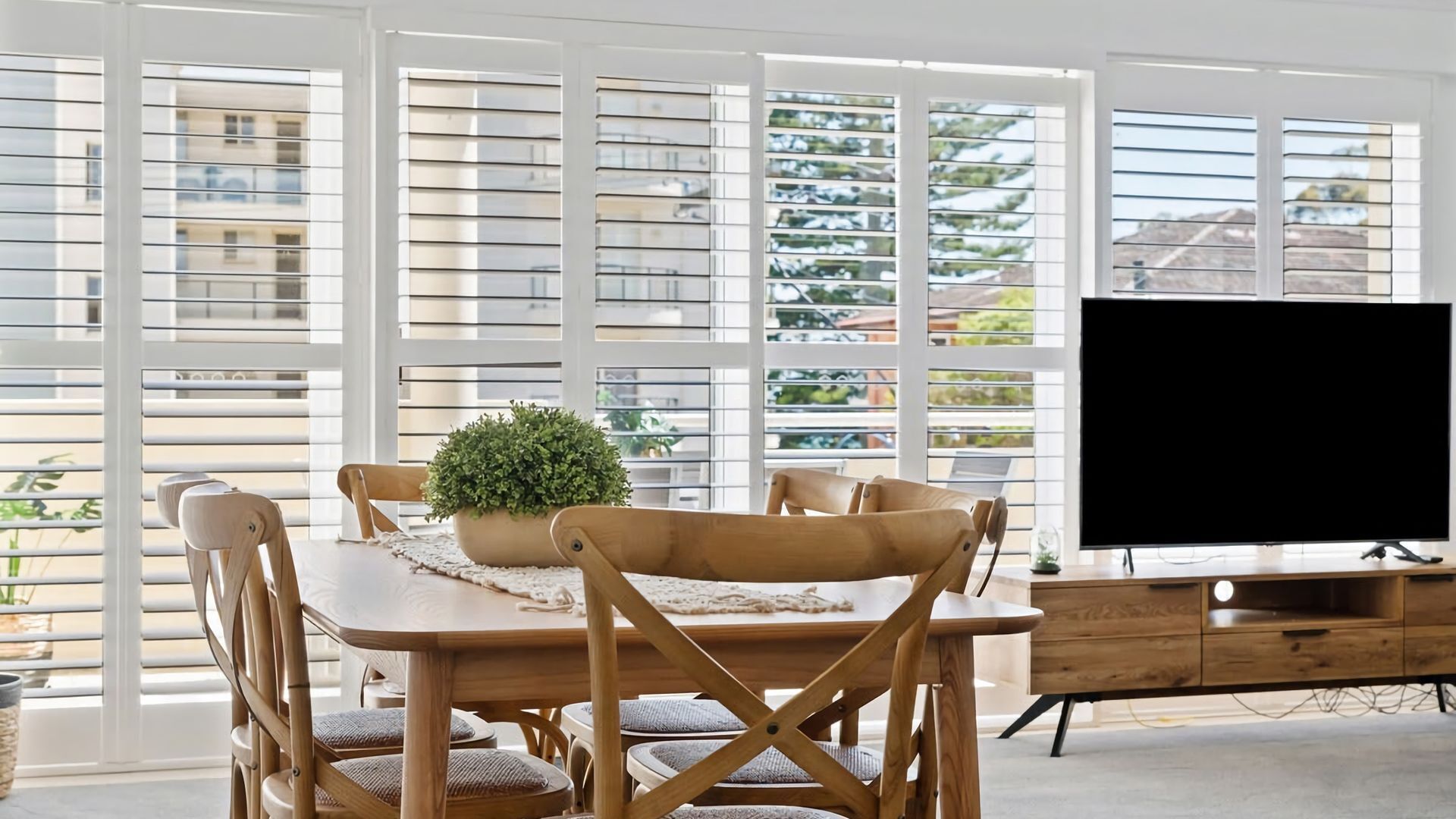 Ein Essbereich mit Holztisch und -stühlen, einem Topfpflanzen und einem Fernseher auf einer Holzkommode.