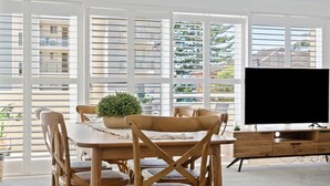 A dining area with a wooden table and chairs, a potted plant, and a TV on a wooden cabinet. - Seashells Sweet Retreat Pool, Walk to Shops & Marina (Nelson Bay)