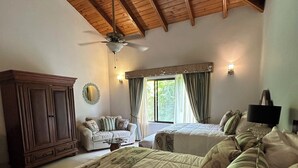 Een slaapkamer met een groot bed, een bank, een houten garderobe, een plafondventilator en een raam met gordijnen.