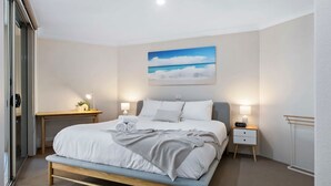 A bedroom with a bed, bedside tables, a nightstand, a painting, and a window. - Coastal Retreat in the Heart of Kiama (Kiama)