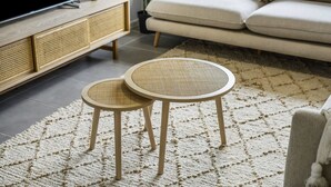 Ein Wohnzimmer mit einem großen Holzschrank, einer Couch und zwei runden Korbtischen auf einem strukturierten Teppich.