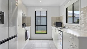 Eine moderne Küche mit weißen Schränken, einem eingebauten Backofen, einer Mikrowelle und einem Fenster mit Jalousien.