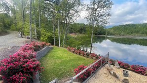 A lakeside garden with a wooden deck, a grassy lawn, and pink flowering bushes. - Private Heated Pool! @ The House on the Cove (Hiawassee)