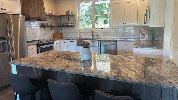 A modern kitchen with a granite island, white cabinetry, and a large window providing natural light. - Private Heated Pool! @ The House on the Cove (Hiawassee)
