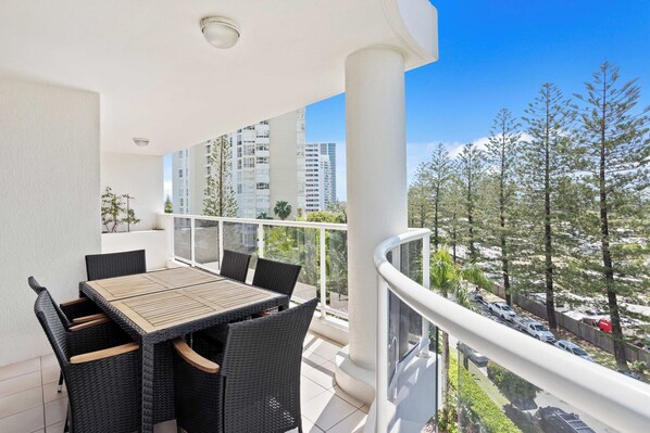A balcony with a table and chairs, overlooking a parking area and trees.