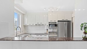 A modern kitchen with white cabinets, stainless steel appliances, and a granite countertop. - Oscar on Main - Heart of Main Beach (Main Beach)