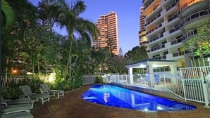 A swimming pool with a white fence, surrounded by palm trees and a multi-story building in the background. - Oscar on Main - Heart of Main Beach (Main Beach)