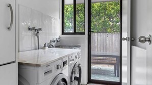 Cocina compacta con lavadora, lavamanos y ventana con vistas a un jardín.