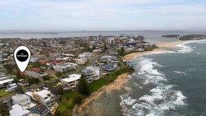 Vista aérea de un pueblo costero con edificios residenciales, una playa y un puente en la distancia.