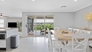 Una cucina moderna con forno a microonde integrato, zona pranzo con sedie bianche e tavolo in legno, e una porta a vetri scorrevoli che dà su un balcone con piante.