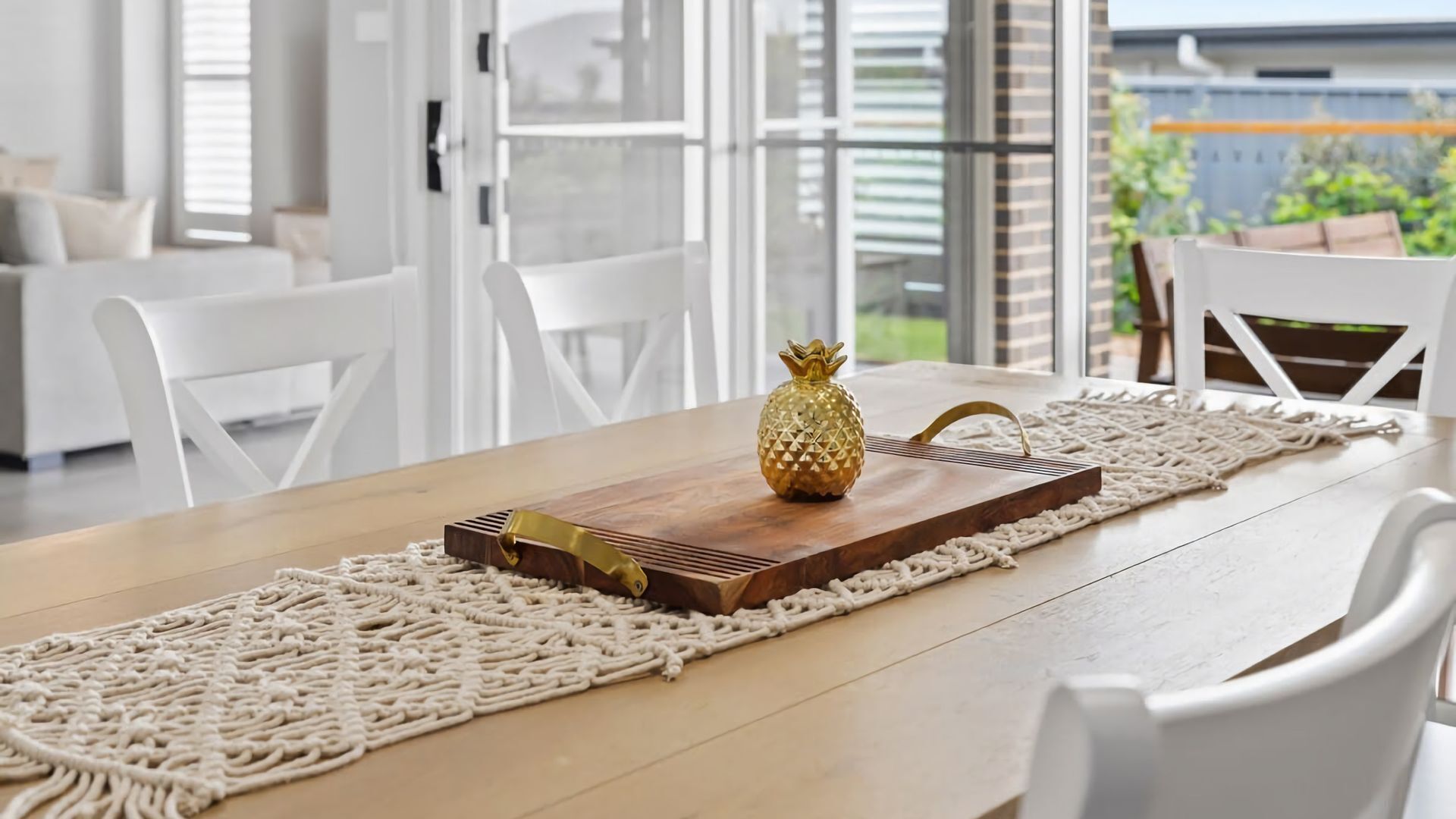 A dining table with a wooden surface, a decorative pineapple centerpiece, and a macrame runner.