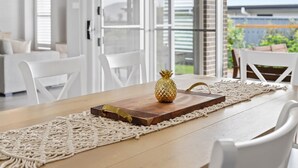 Un tavolo da pranzo con piano in legno, un centrotavola decorativo con ananas e un runner in macramè.