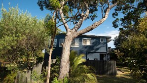 A two-story house with a dark blue exterior, surrounded by lush greenery and trees. - Broulee Beachfront Bliss - Near the Waves (Broulee)