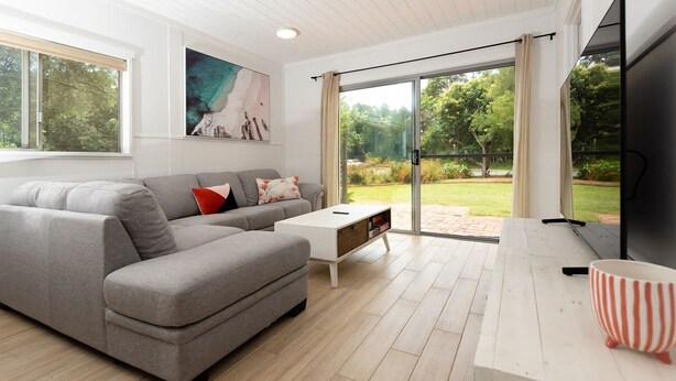 A modern living room with a grey sectional sofa, a white coffee table, and a large flat-screen TV. - Broulee Beachfront Bliss - Near the Waves (Broulee)