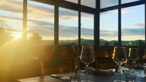 A table set for dining with empty glasses, a napkin, and a menu, overlooking a scenic landscape with mountains and a sunset. - Broulee Beachfront Bliss - Near the Waves (Broulee)