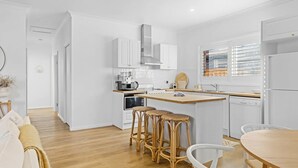 A modern kitchen with white cabinets, a central island with stools, a coffee machine, and a window with blinds.