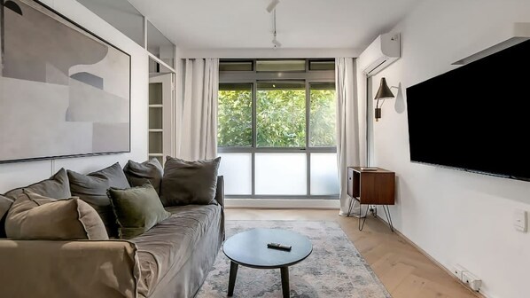 A modern living room with a sofa, a coffee table, a TV, and a large window with curtains.