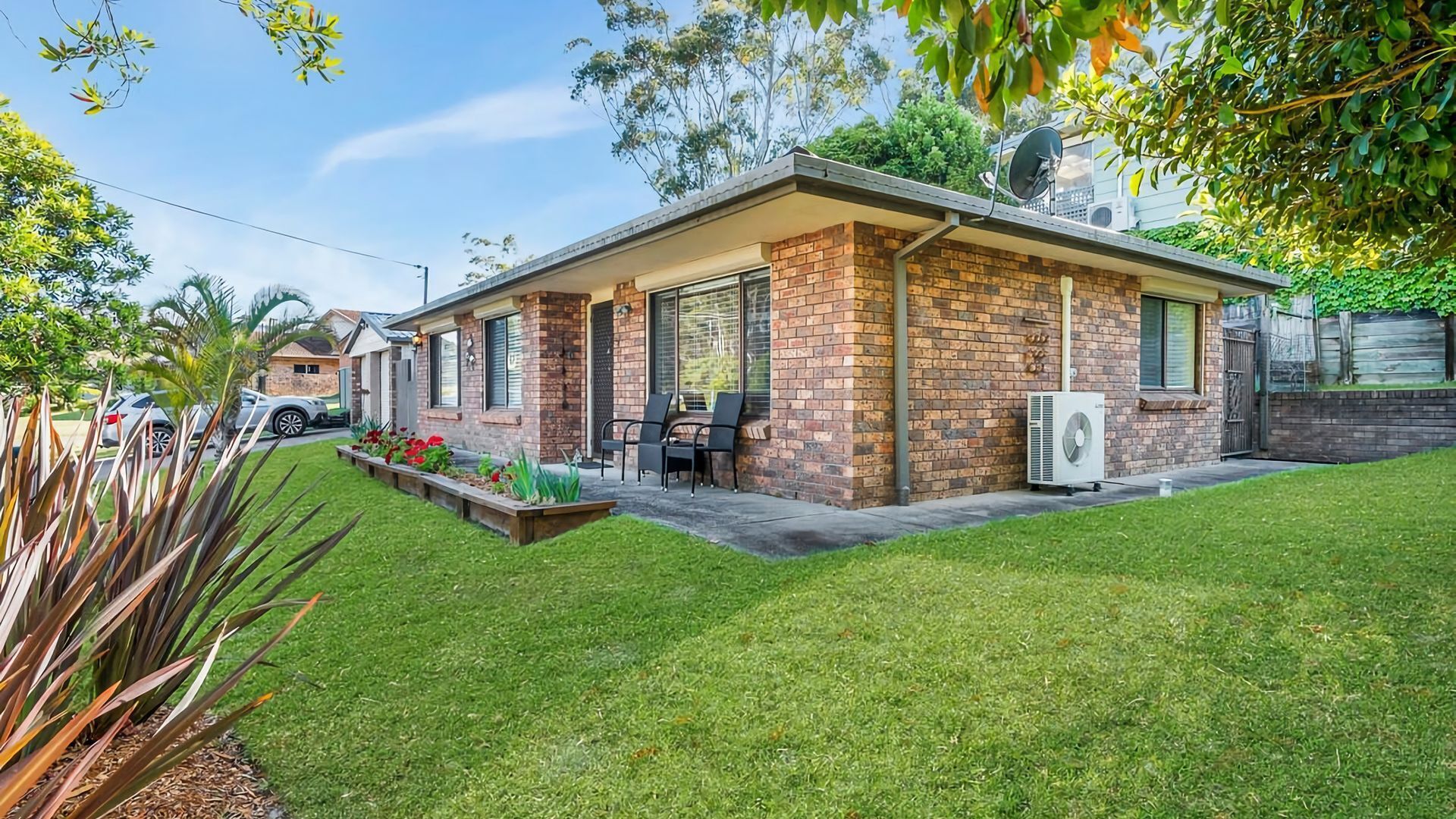 Ein modernes Einfamilienhaus mit Backsteinfassade, einer kleinen Terrasse mit Gartenmöbeln und einem gepflegten Rasen.