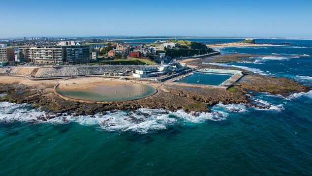 Vue aérienne d’une zone côtière avec une plage rocheuse, une piscine et une promenade.