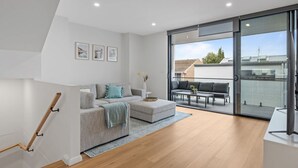 En moderne stue med en grå sofa, et sofabord og en balkon med en sort sofa og bord.