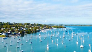 A coastal marina with numerous sailboats docked, surrounded by residential buildings and greenery.