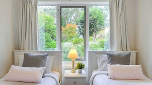 Una habitación con dos camas, una mesita de noche con lámpara y una ventana con cortinas.