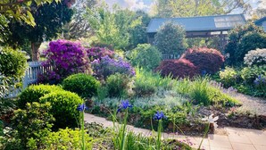 Un jardín con diversas plantas y flores, una cerca de madera y un edificio con techo azul.
