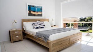 A modern bedroom with a wooden bed, white bedding, and a view of greenery outside. - Blissful Stay Moments From the Beach (Surf Beach)