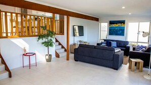 A spacious living area with a staircase, a large grey sofa, and a painting on the wall. - Blissful Stay Moments From the Beach (Surf Beach)