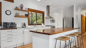 Una cucina moderna con mobili bianchi, un piano di lavoro in legno, un piano cottura integrato e un'ampia finestra.