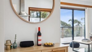 Un soggiorno moderno con un tavolino consolle in legno, una bottiglia di vino, una piccola pianta e vista all'aperto tramite un'ampia finestra.