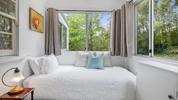 Relax in this serene bedroom with a large bed, desk, and window offering a view of lush greenery.