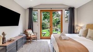 Una habitación de hotel con una cama, un escritorio, una silla, un televisor y un ventanal corredero a un jardín.