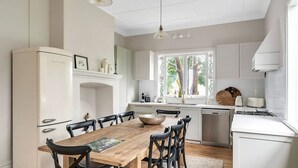 Una cocina moderna con muebles blancos, una mesa de comedor de madera y un amplio ventanal con vistas a árboles.