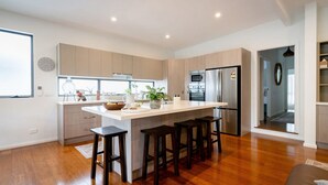 A modern kitchen with a central island, wooden cabinets, stainless steel appliances, and a large window. - Kilaben Bay Escape - Minutes to the Water (Kilaben Bay)
