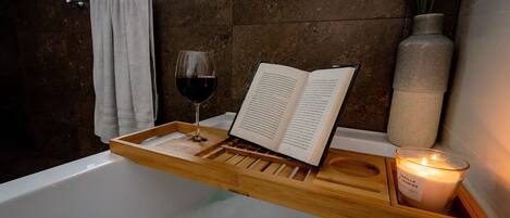 A wooden tray with a book and a glass of red wine on a bathtub.