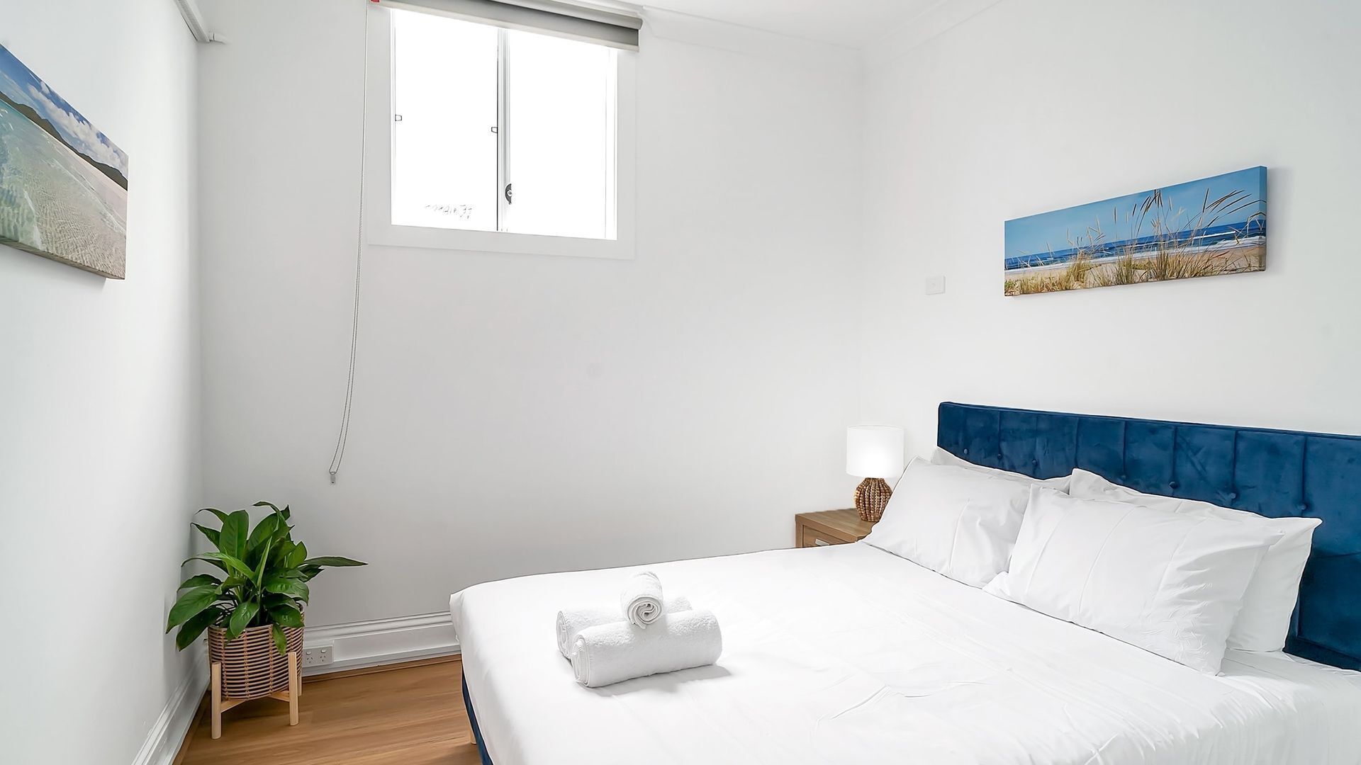Un dormitorio con una cama, una ventana, una planta y un cuadro en la pared.