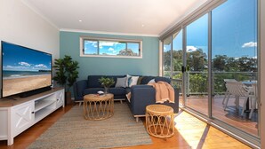 A modern living room with a large TV, a sofa, a coffee table, and a balcony with outdoor furniture.