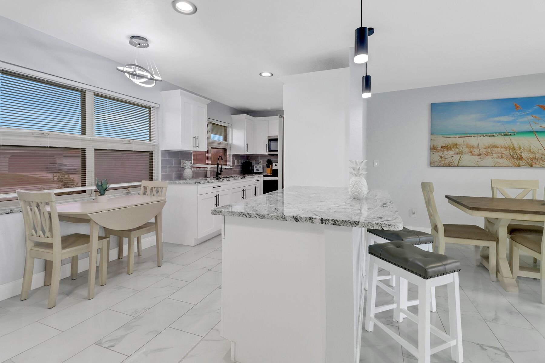 Une cuisine moderne avec des meubles blancs, un îlot central et un coin repas comprenant des chaises et une table en bois.