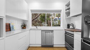 Una cocina moderna con armarios blancos, lavavajillas, horno, refrigerador y ventana con vista a un jardín.