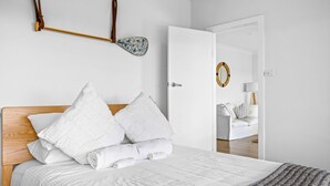Un dormitorio con cabecera de madera, ropa de cama blanca y vistas a una habitación contigua con sofá blanco y espejo.