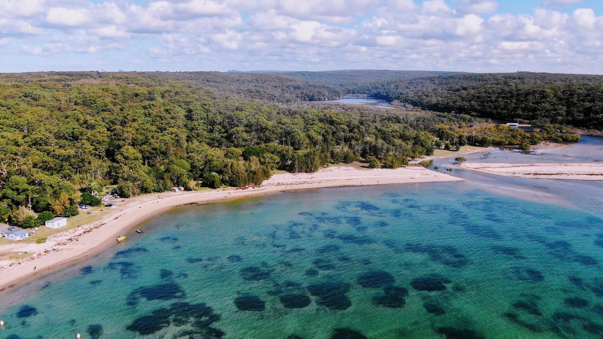 A coastal landscape with a beach, clear water, and dense forest.