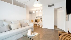 A modern living room with a white sofa, a glass coffee table, and a dining area with a wooden table and chairs. - The Little Bondi Base (Bondi Junction)